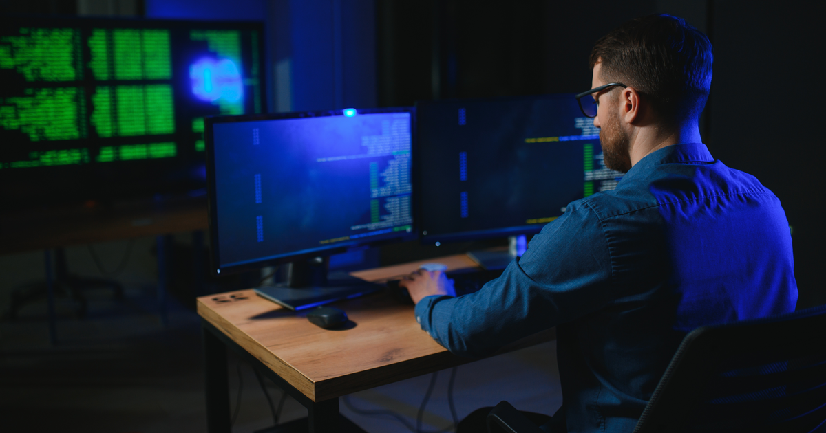 Developer reviewing PowerShell code across several monitors at a blue-lit workstation.