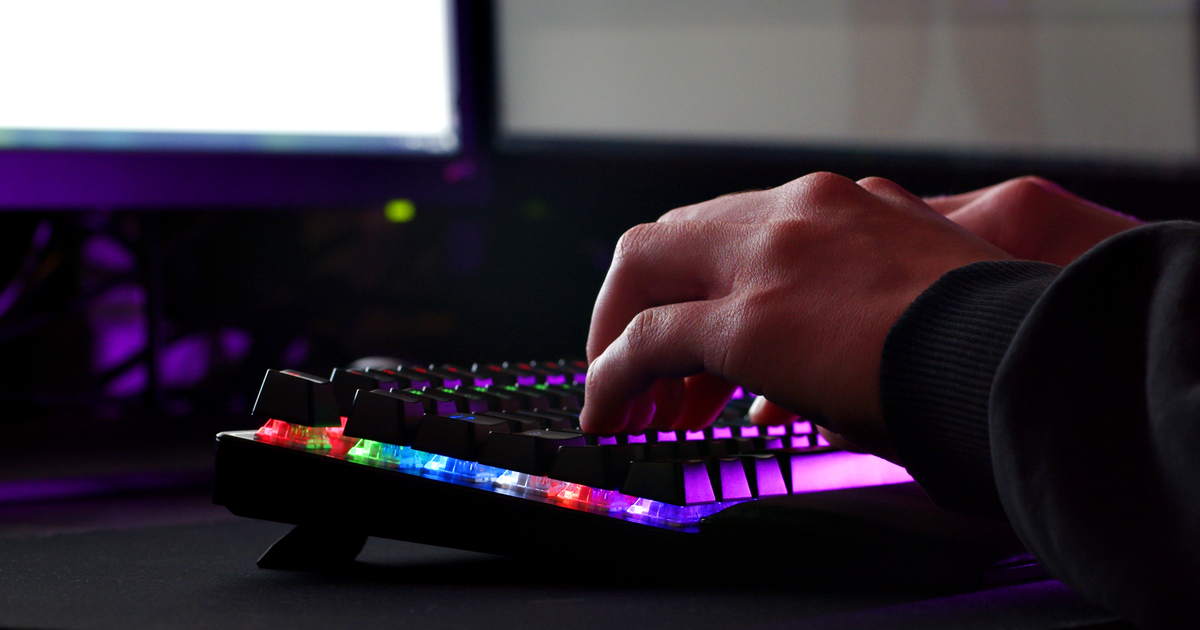 Person typing on a backlit keyboard while reviewing code on two computer monitors.